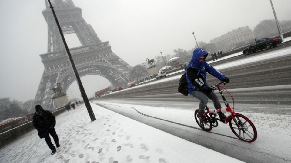 Cyklista prechádza okolo Eiffelovej veže počas sneženia v Paríži.