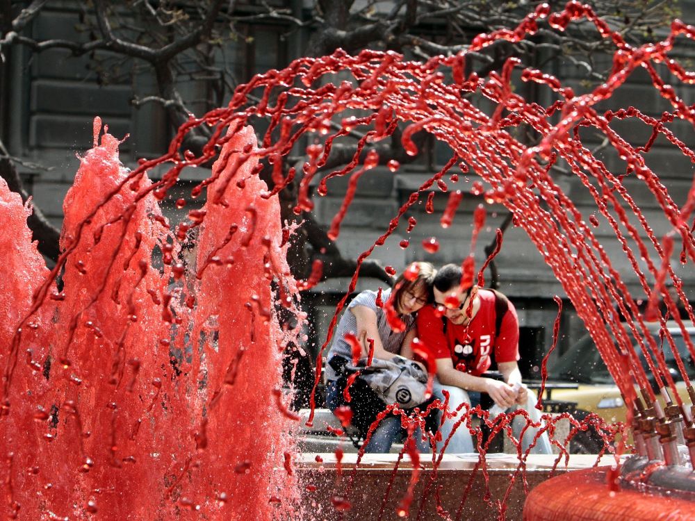 Párik sedí na lavičke neďaleko fontány, ktorej voda je sfarbená dočervena, 16. apríla 2010, Bukurešť. Všetky fontány v centre mesta mali takto sfarbenú vodu pri príležitosti Svetového dňa hemofílie.