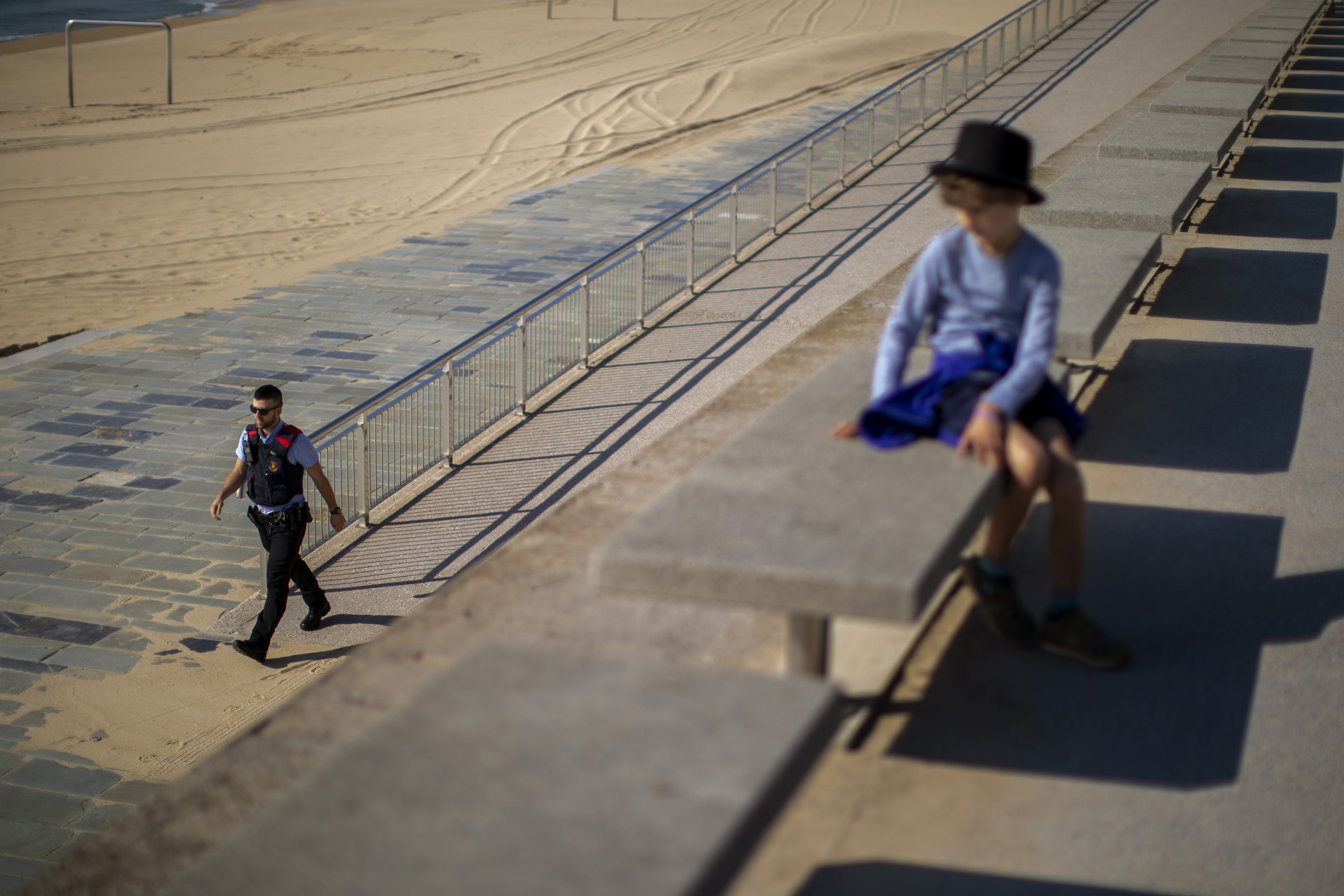 Na snímke sa dieťa pozerá na policajta hliadkujúceho na promenáde na pláži, kde je zakázaný vstup kvôli karanténe v Barcelone v Španielsku v nedeľu 26. apríla 2020.