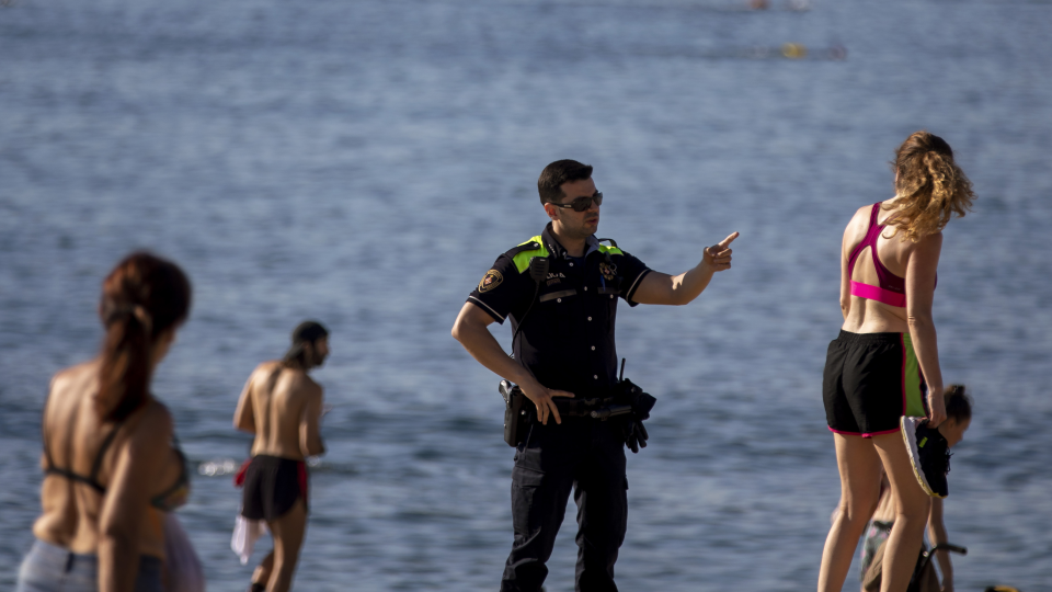 llustračná snímka, policajt upozorňuje počas hliadkovania ľudí, ktorí sa kúpu a opaľujú na pláži v Barcelone 20. mája 2020, aby si nesadali.