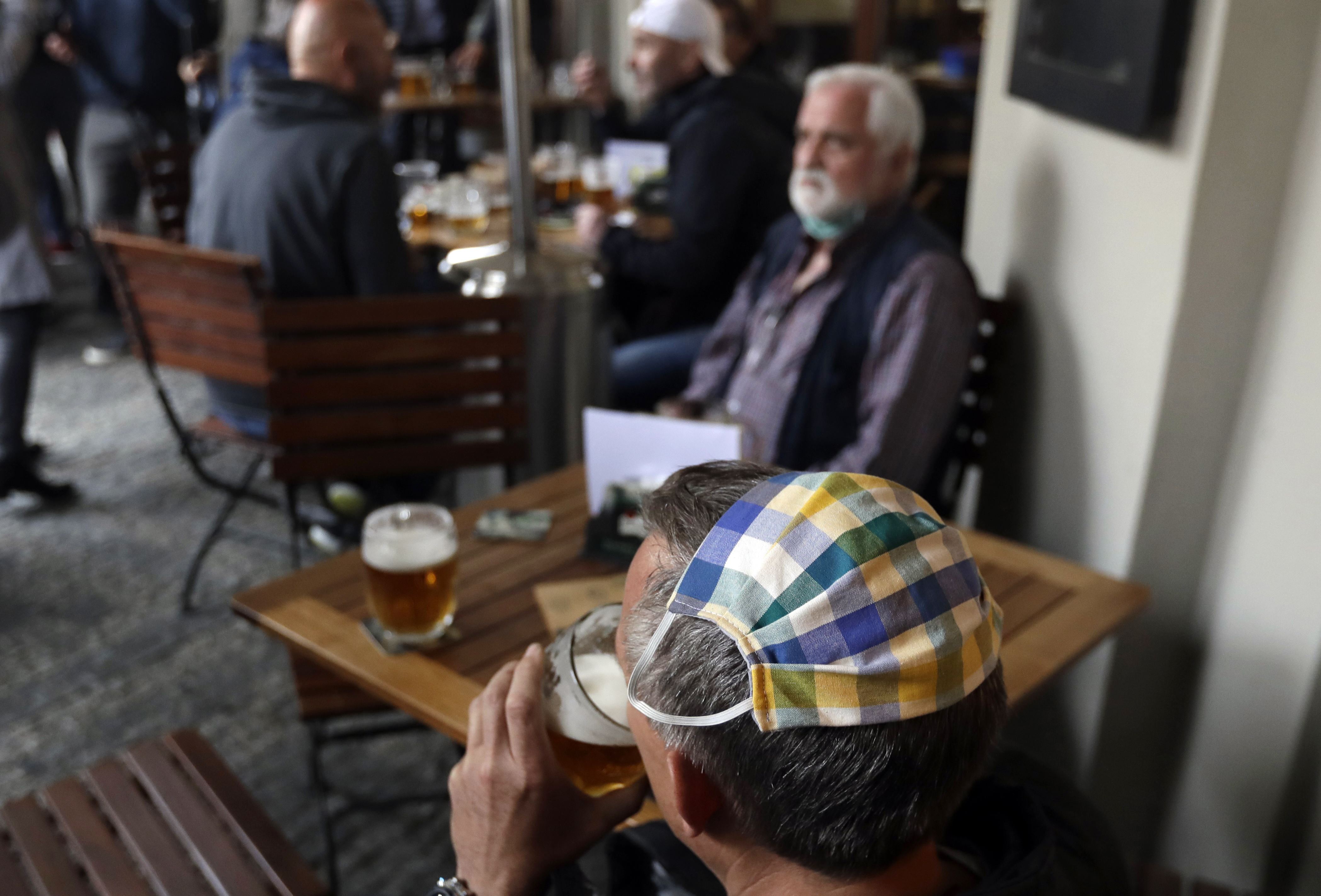 Muž s ochranným rúškom na zabránenie šíreniu nového koronavírusu na hlave pije pivo na letnej terase reštaurácie v Prahe 17. mája 2020.