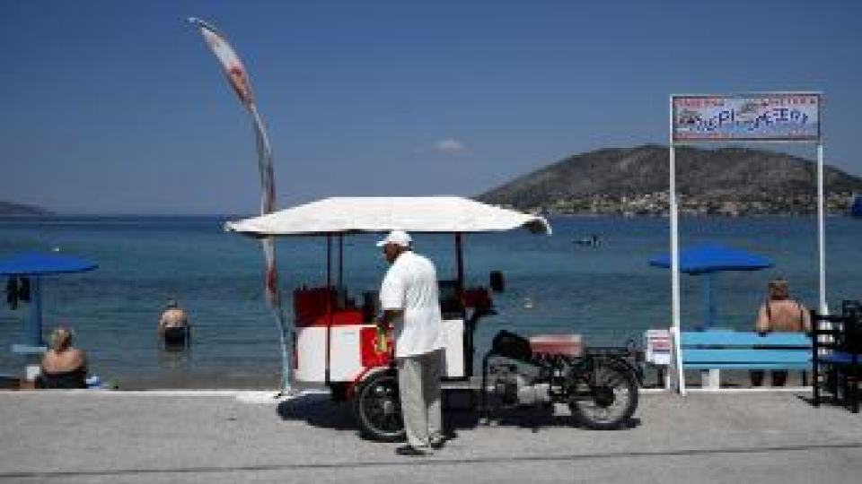 Pouličný predavač zmrzliny fajčí cigaretu a čaká na zákazníkov vedľa pláže na gréckom ostrove Salamína.