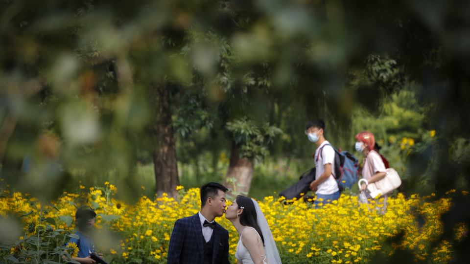 Ľudia s ochrannými rúškami kráčajú okolo mladomanželov, ktorí pózujú fotografovi v Olympijskom parku v Pekingu 2. júla 2020.