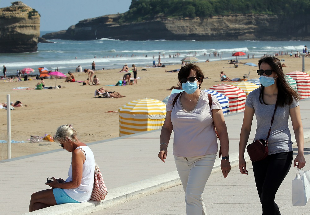 Ľudia s ochrannými rúškami kráčajú vedľa pláže v meste Biarritz v juhozápadnom Francúzsku v utorok 21. júla 2020.