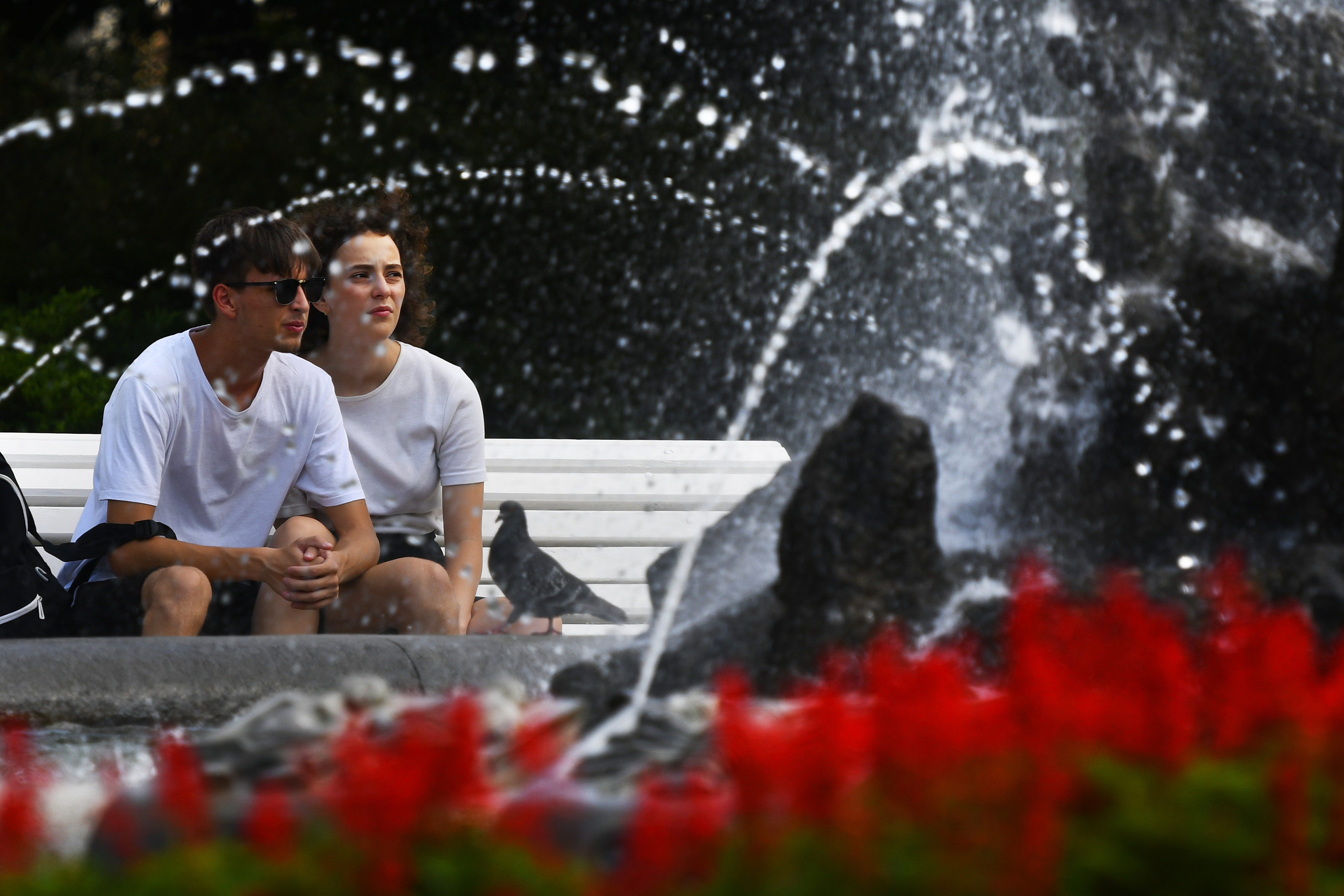 Pár sedí na lavičke pri fontáne počas horúcich letných dní v centre Košíc.