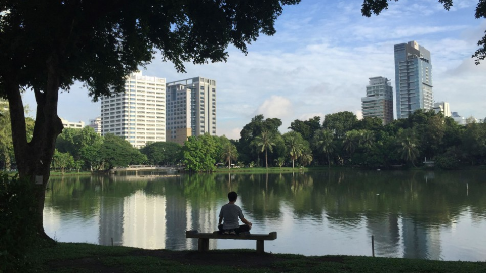 Muž medituje na lavičke pri jazere v Lumphini Park v Bankoku v Thajsku. 